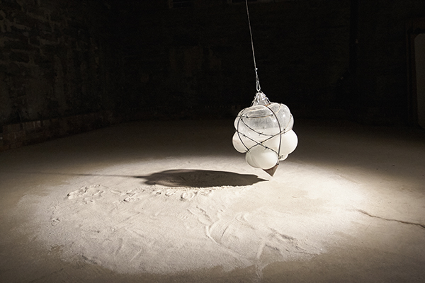 A blown-glass pendulum sweeps across a circle of sand.