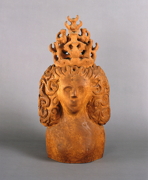A sculpted bust of a woman with intricate curly hair and a large, ornate crown, set against a plain gray background.