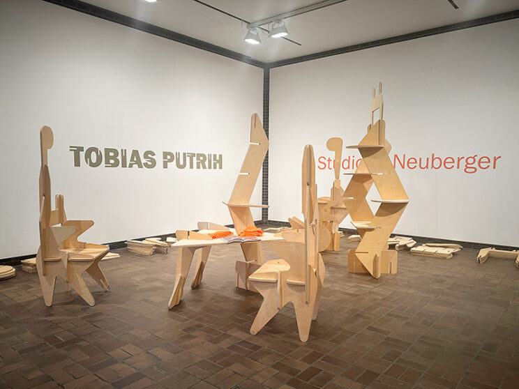 A gallery with wooden slotted shapes, some assembled into furniture and others in piles on the floor.